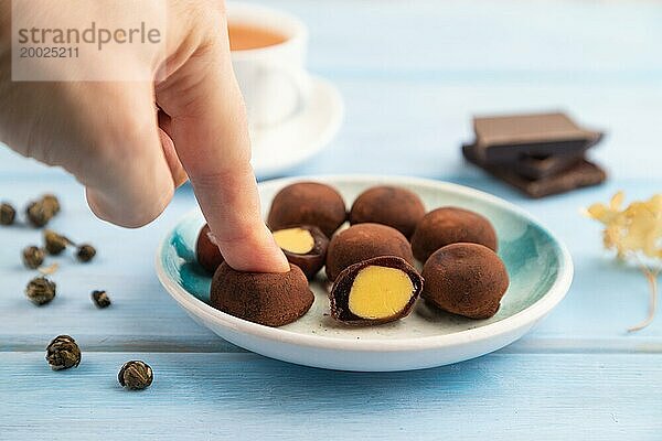 Japanischer Reis süße Brötchen Schokolade Mochi gefüllt mit Sahne und Tasse grüner Tee mit der Hand auf blauen hölzernen Hintergrund. Seitenansicht  Nahaufnahme  selektiver Fokus