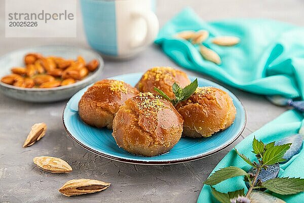 Hausgemachtes traditionelles türkisches Dessert Sekerpare mit Mandeln und Honig  Tasse grüner Tee auf grauem Betonhintergrund und blauem Textil. Seitenansicht  selektiver Fokus