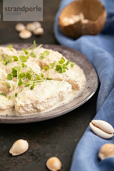 Geschmorte Hühnerfilets mit Kokosmilchsauce und Rucola Mikrogrün auf schwarzem Betonhintergrund und blauem Leinentuch. Seitenansicht  Nahaufnahme  selektiver Fokus