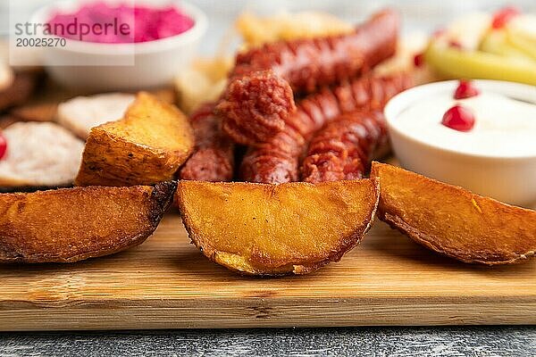 Snacks: Würstchen  Toast  Sauerkraut  marinierte Zwiebeln und Gurken  gebackene Kartoffeln auf einem Schneidebrett auf einem grauen Holzhintergrund. Seitenansicht  Nahaufnahme  selektiver Fokus