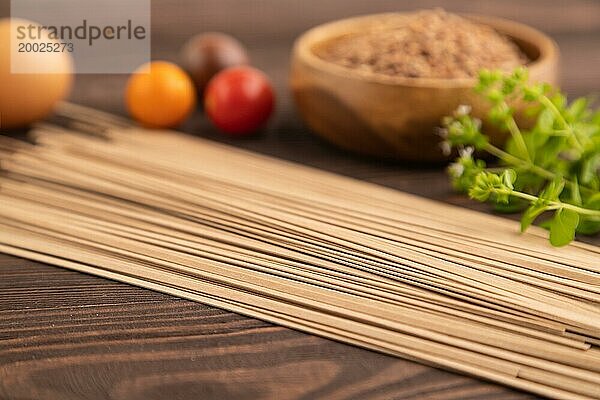 Japanische Buchweizen Soba Nudeln mit Tomaten  Eiern  Gewürzen  Kräutern auf braunem Holzhintergrund. Seitenansicht  Nahaufnahme  selektiver Fokus