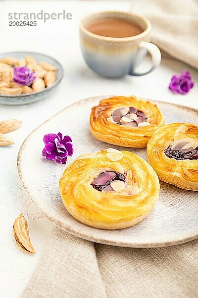 Kleine Käsekuchen mit Marmelade und Mandeln mit einer Tasse Kaffee auf weißem Betonhintergrund und Leinenstoff. Seitenansicht  Nahaufnahme  selektiver Fokus