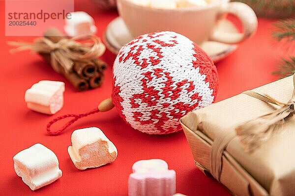 Weihnachten oder Neujahr Zusammensetzung. Dekorationen  Box  Zimt  gestrickte Kugeln  Tanne und Fichte Zweige  Tasse Kaffee  auf einem roten Papier Hintergrund. Seitenansicht  Nahaufnahme  selektiver Fokus