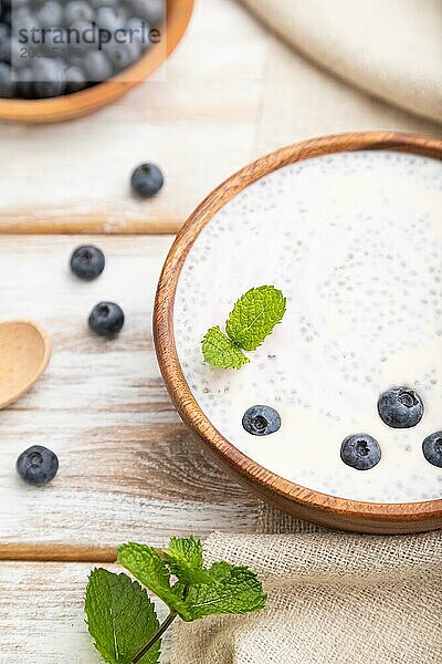 Joghurt mit Blaubeeren in einer Holzschale auf weißem Holzhintergrund und Leinenstoff. Seitenansicht  Nahaufnahme  selektiver Fokus