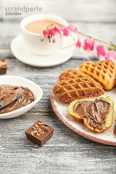 Hausgemachte Waffel mit Schokoladenbutter und Tasse Kaffee auf einem grauen Holzhintergrund. Seitenansicht  selektiver Fokus  Nahaufnahme