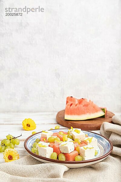 Vegetarischer Salat mit Wassermelone  Fetakäse und Trauben auf blauem Keramikteller auf weißem Holzhintergrund und Leinentuch. Seitenansicht  Kopierraum  selektiver Fokus