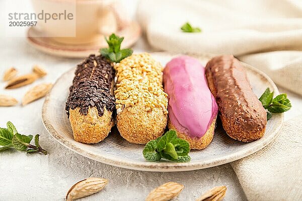 Set von Eclair  traditionelles französisches Dessert und Tasse Kaffee auf grauem Betonhintergrund und Leinenstoff. Seitenansicht  Nahaufnahme  selektiver Fokus  Stillleben. Frühstück  Morgen  Konzept