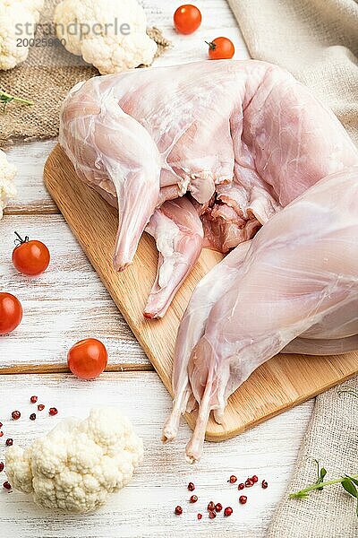 Ganzes rohes Kaninchen mit Blumenkohl  Tomaten und Gewürzen auf einem weißen Holzhintergrund und Leinenstoff. Seitenansicht  Nahaufnahme  selektiver Fokus