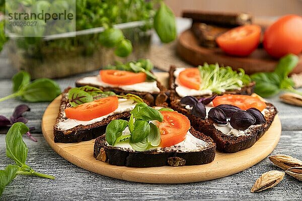 Korn Roggenbrot Sandwiches mit Frischkäse  Tomaten und Basilikum microgreen auf grauem hölzernen Hintergrund und Leinen Textil. Seitenansicht  Nahaufnahme  selektiven Fokus