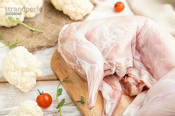 Ganzes rohes Kaninchen mit Blumenkohl  Tomaten und Gewürzen auf einem weißen Holzhintergrund und Leinenstoff. Seitenansicht  Nahaufnahme  selektiver Fokus