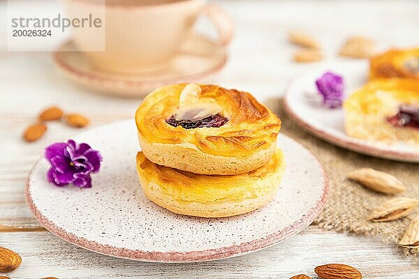 Kleine Käsekuchen mit Marmelade und Mandeln mit einer Tasse Kaffee auf einem weißen Holzhintergrund und Leinenstoff. Seitenansicht  Nahaufnahme  selektiver Fokus