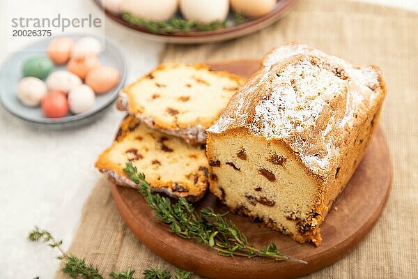 Hausgemachter Osterkuchen mit Rosinen und Eiern auf einem Teller auf einem grauen Betonhintergrund und Leinenstoff. Seitenansicht  selektiver Fokus  Nahaufnahme