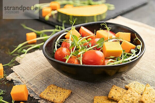 Vegetarischer Gemüsesalat aus Tomaten  Kürbis  mikrogrünen Erbsensprossen auf schwarzem Betonhintergrund und Leinentuch. Seitenansicht  Nahaufnahme  selektiver Fokus