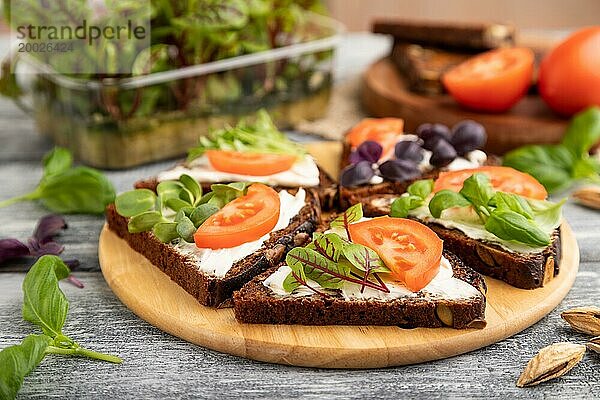 Roggenkornbrot Sandwiches mit Frischkäse  Tomaten und Sauerampfer Mikrogrün auf grauem Holzhintergrund und Leinentextil. Seitenansicht  Nahaufnahme  selektiver Fokus