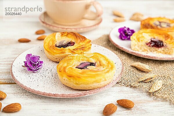 Kleine Käsekuchen mit Marmelade und Mandeln mit einer Tasse Kaffee auf einem weißen Holzhintergrund und Leinenstoff. Seitenansicht  Nahaufnahme  selektiver Fokus