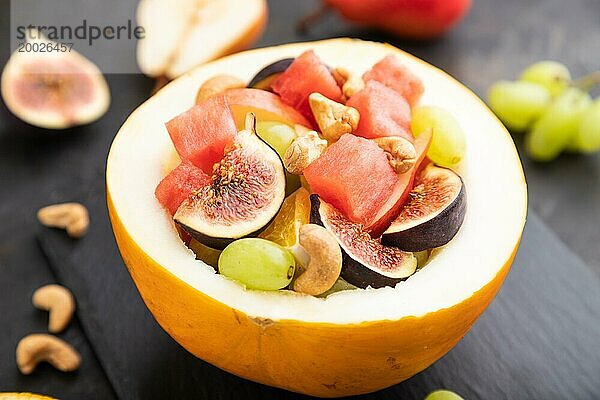 Vegetarischer Obstsalat aus Wassermelone  Trauben  Feigen  Birne  Orange  Cashew auf Schieferplatte auf einem schwarzen Betonhintergrund. Seitenansicht  Nahaufnahme  selektiver Fokus