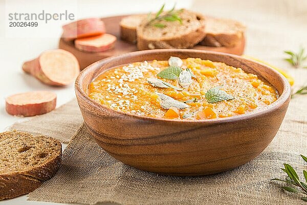 Süßkartoffel oder Batatencremesuppe mit Sesam in einer Holzschale auf weißem Holzhintergrund mit Leinenstoff. Seitenansicht  Nahaufnahme  selektiver Fokus