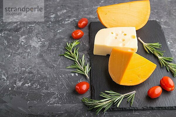 Verschiedene Käsesorten mit Rosmarin und Tomaten auf einer schwarzen Schiefertafel auf einem schwarzen Betonhintergrund. Seitenansicht  Nahaufnahme  Kopierraum  selektiver Fokus