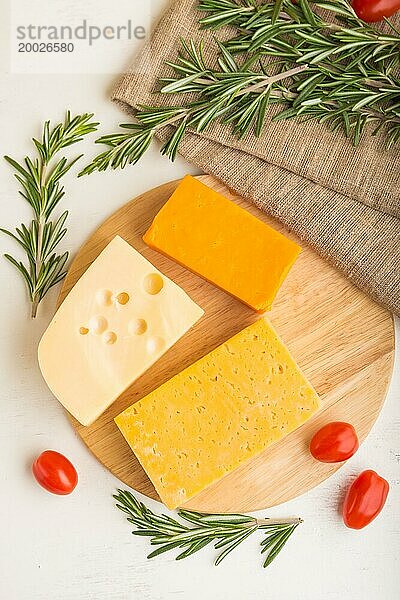 Verschiedene Käsesorten mit Rosmarin und Tomaten auf Holzbrett auf weißem Holzhintergrund und Leinenstoff. Draufsicht  Nahaufnahme  flach gelegt