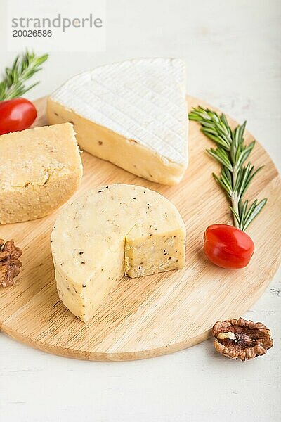 Cheddar und verschiedene Käsesorten mit Rosmarin und Tomaten auf einem Holzbrett vor einem weißen Holzhintergrund. Seitenansicht  Nahaufnahme  selektiver Fokus