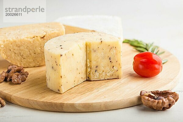 Cheddar und verschiedene Käsesorten mit Rosmarin und Tomaten auf einem Holzbrett vor einem weißen Holzhintergrund. Seitenansicht  Nahaufnahme  selektiver Fokus