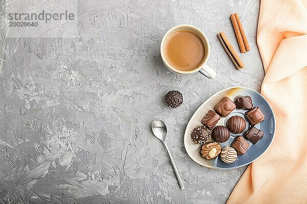 Verschiedene Schokoladenbonbons und eine Tasse Kaffee auf grauem Betonhintergrund und orangefarbenem Textil. Draufsicht  Flat Lay  Copy Space