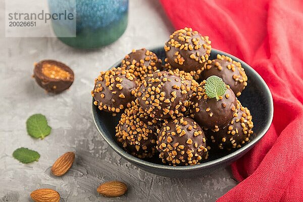 Karamellbonbons mit Mandeln und einer Tasse Kaffee auf einem grauen Betonhintergrund und rotem Stoff. Seitenansicht  Nahaufnahme  selektiver Fokus