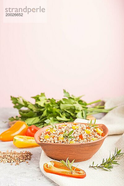 Buchweizenbrei mit Gemüse in Tonschale auf grauem und rosa Hintergrund und Leinenstoff. Seitenansicht  selektiver Fokus  Kopierbereich. Russische traditionelle Küche