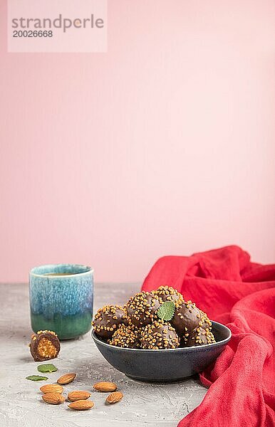 Karamellbonbons mit Mandeln und einer Tasse Kaffee auf grauem und rosa Hintergrund und rotem Stoff. Seitenansicht  Kopierraum  selektiver Fokus