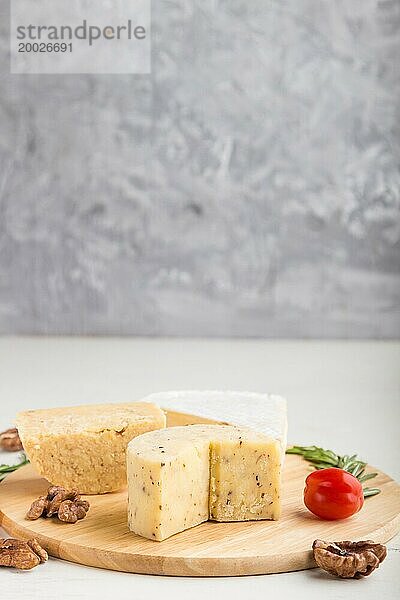 Cheddar und verschiedene Käsesorten mit Rosmarin und Tomaten auf einem Holzbrett auf einem grauen und weißen Hintergrund. Seitenansicht  Kopierraum  selektiver Fokus