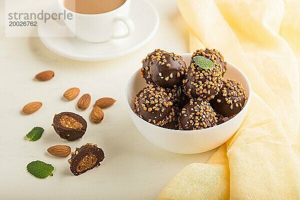 Karamellbonbons mit Mandeln und einer Tasse Kaffee auf einem weißen Holzhintergrund und gelbem Stoff. Seitenansicht  Nahaufnahme  selektiver Fokus