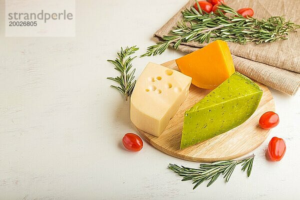 Grüner Basilikumkäse und verschiedene Käsesorten mit Rosmarin und Tomaten auf einem Holzbrett auf einem weißen Holzhintergrund. Seitenansicht  Kopierraum  selektiver Fokus