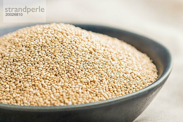 Blaue Keramikschale mit rohen weißen Quinoa Samen auf grauem Betonhintergrund und Leinenstoff. Seitenansicht  Nahaufnahme  selektiver Fokus