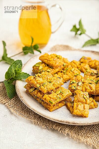 Traditionelles iranisches Dessert Sohan mit einem Glas grünem Tee auf einem grauen Betonhintergrund und Leinenstoff. Seitenansicht  Nahaufnahme  selektiver Fokus