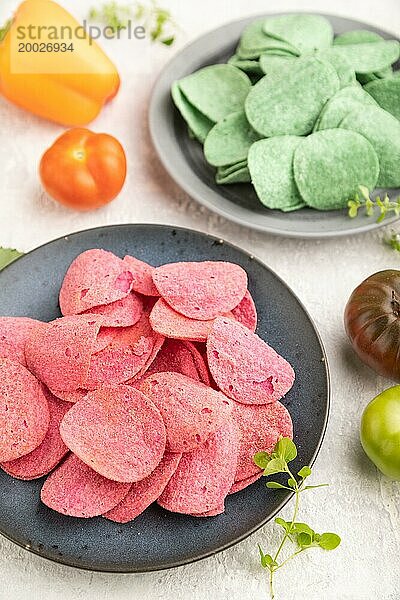 Grüne und rote Kartoffelchips mit Kräutern und Tomaten auf grauem Betonhintergrund. Seitenansicht  Nahaufnahme  selektiver Fokus