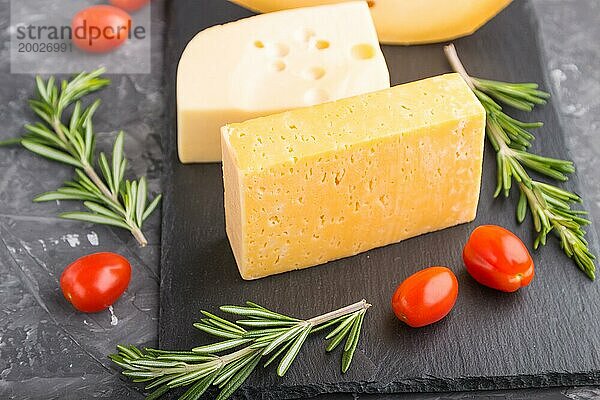 Verschiedene Käsesorten mit Rosmarin und Tomaten auf einer schwarzen Schiefertafel auf einem schwarzen Betonhintergrund. Seitenansicht  Nahaufnahme  selektiver Fokus