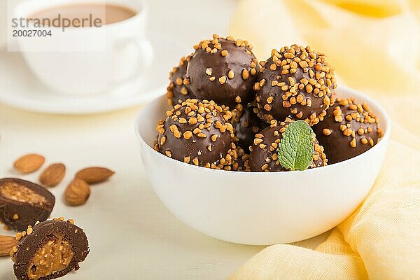 Karamellbonbons mit Mandeln und einer Tasse Kaffee auf einem weißen Holzhintergrund und gelbem Stoff. Seitenansicht  Nahaufnahme  selektiver Fokus