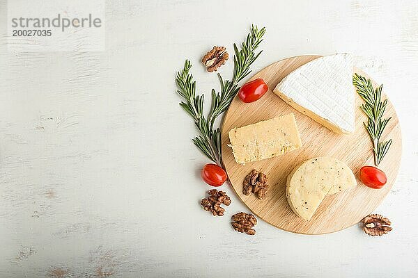 Cheddar und verschiedene Käsesorten mit Rosmarin und Tomaten auf einem Holzbrett auf einem weißen Holzhintergrund. Draufsicht  flat lay  copy space