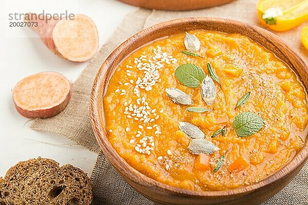 Süßkartoffel oder Batatencremesuppe mit Sesam in einer Holzschale auf weißem Holzhintergrund mit Leinenstoff. Seitenansicht  Nahaufnahme  selektiver Fokus