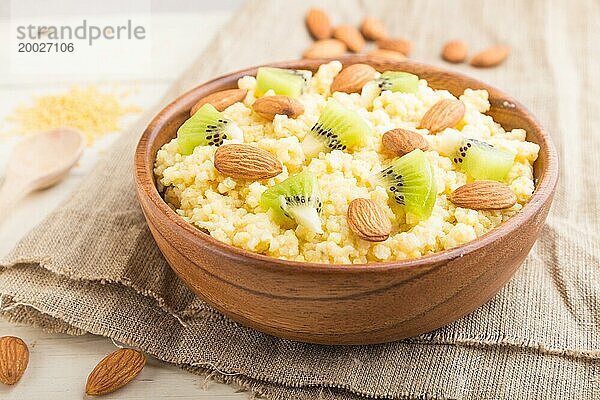 Hirsebrei mit Kiwi und Mandeln in einer Holzschale auf weißem Holzhintergrund und Leinenstoff. Seitenansicht  Nahaufnahme  selektiver Fokus