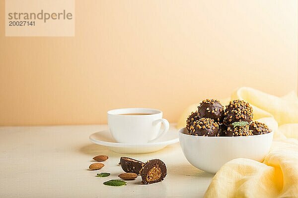 Karamellbonbons mit Mandeln und einer Tasse Kaffee auf weißem und orangefarbenem Hintergrund und gelbem Textil. Seitenansicht  Kopierraum  selektiver Fokus