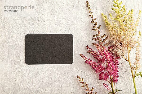 Schwarzes Papier Visitenkarte Mockup mit lila Astilbe Blumen auf grauem Beton Hintergrund. Leer  Draufsicht  Kopierraum  Stillleben. Frühlingskonzept