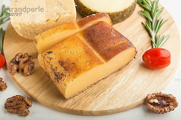 Geräucherter Käse und verschiedene Käsesorten mit Rosmarin und Tomaten auf einem Holzbrett auf einem weißen Holzhintergrund. Seitenansicht  Nahaufnahme  selektiver Fokus