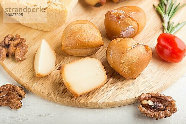 Geräucherter Käse und verschiedene Käsesorten mit Rosmarin und Tomaten auf einem Holzbrett auf einem weißen Holzhintergrund. Seitenansicht  Nahaufnahme  selektiver Fokus