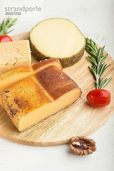 Geräucherter Käse und verschiedene Käsesorten mit Rosmarin und Tomaten auf einem Holzbrett auf einem weißen Holzhintergrund. Seitenansicht  Nahaufnahme  selektiver Fokus