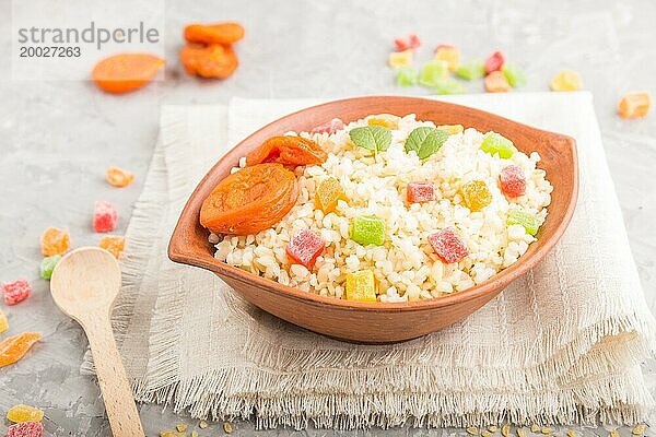 Bulgur Brei mit getrockneten Aprikosen und kandierten Früchten in einer Tonschüssel auf grauem Betonhintergrund und Leinentextil. Seitenansicht  Nahaufnahme  selektiver Fokus. Traditionelle türkische Küche