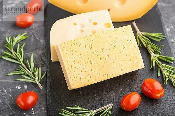 Verschiedene Käsesorten mit Rosmarin und Tomaten auf einer schwarzen Schiefertafel auf einem schwarzen Betonhintergrund. Seitenansicht  Nahaufnahme  selektiver Fokus