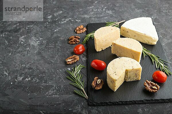 Cheddar Käse und verschiedene Käsesorten mit Rosmarin und Tomaten auf einer schwarzen Schiefertafel auf einem schwarzen Betonhintergrund. Seitenansicht  Kopierraum  selektiver Fokus