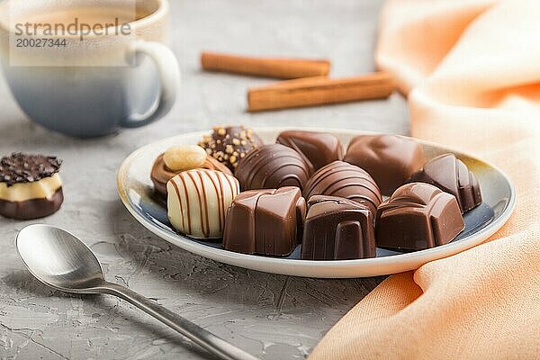 Verschiedene Schokoladenbonbons und eine Tasse Kaffee auf einem grauen Betonhintergrund und orangefarbenem Textil. Seitenansicht  Nahaufnahme  selektiver Fokus