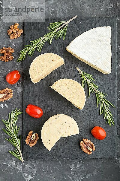 Cheddar Käse und verschiedene Käsesorten mit Rosmarin und Tomaten auf einer schwarzen Schiefertafel auf einem schwarzen Betonhintergrund. Draufsicht  Nahaufnahme  Kopierraum